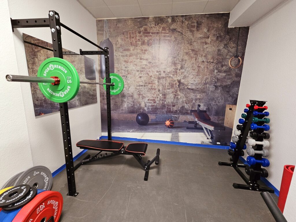 Trainingsbereich der Therapiepraxis Tom Gundlach mit Rack, Langhantel, Hantelbank und Kurzhanteln
