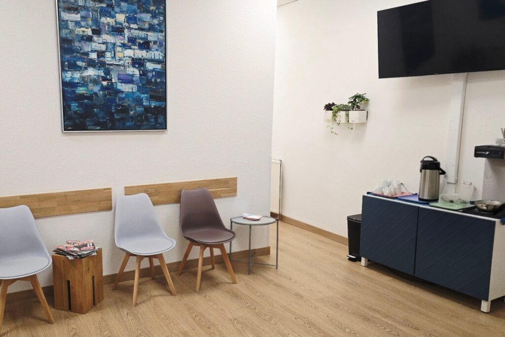 Wartebereich der Therapiepraxis Tom Gundlach in Berlin mit Stühlen, Wandbild und Getränkestation